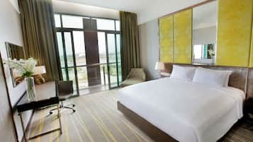 Habitación de hotel con una cama grande, un escritorio con silla, un espejo y vistas a un paisaje a través de amplios ventanales.