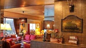 Vestíbulo de hotel con mostrador de recepción, asientos rojos y un gran cuadro con una imagen de un tren.