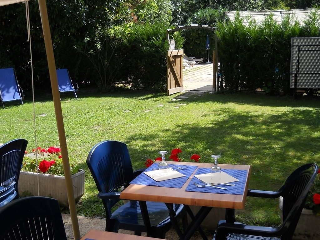 Een terras buiten met een tafel voor twee personen, omringd door stoelen, en een pad dat naar een houten poort leidt.