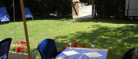 Een terras buiten met een tafel voor twee personen, omringd door stoelen, en een pad dat naar een houten poort leidt.