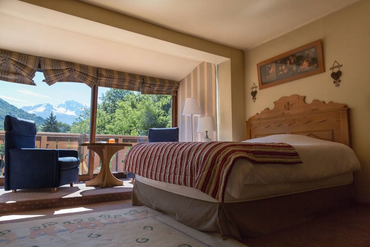 Un dormitorio con una cama grande, una silla, una mesita y vistas a las montañas.