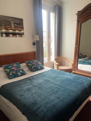 A hotel room with a bed, a chair, a window, and a mirror. - Hôtel Verlaine (Paris)