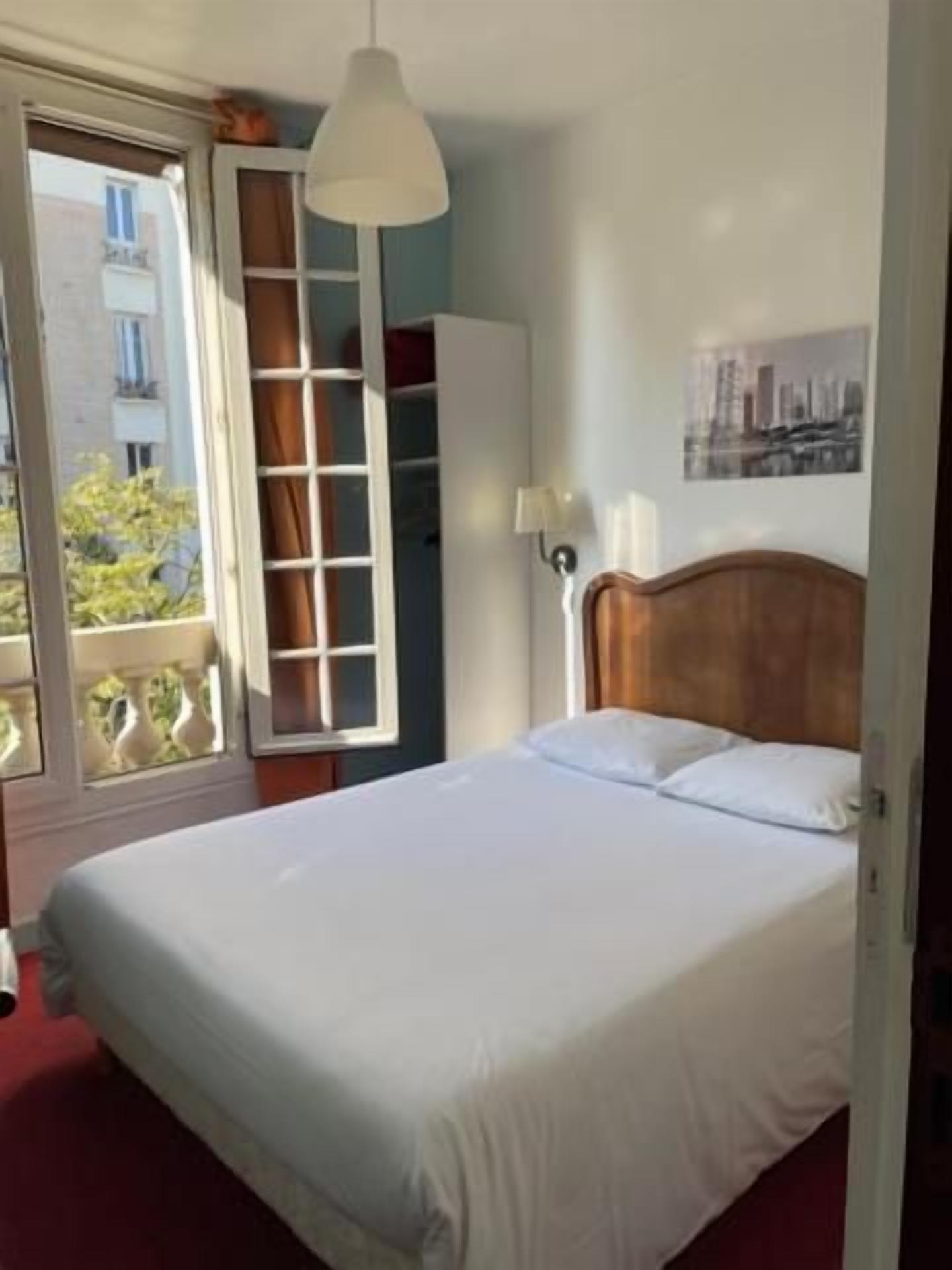 Un dormitorio con cama, armario, ventana y una lámpara fijada a la pared.