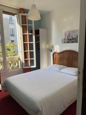 A bedroom with a bed, a wardrobe, a window, and a wall-mounted lamp. - Hôtel Verlaine (Paris)