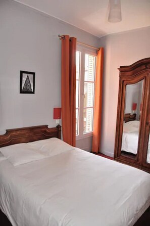 Un dormitorio con una cama grande, una ventana con cortinas, un espejo y un cuadro enmarcado en la pared.