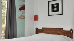 Une chambre à coucher avec un lit en bois, une armoire, un tableau encadré au mur et une fenêtre avec un rideau.