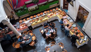 A dining area with multiple tables and chairs, a buffet setup with various food items, and a green wall with plants. - Del Carmen Concept Hotel (Guadalajara)