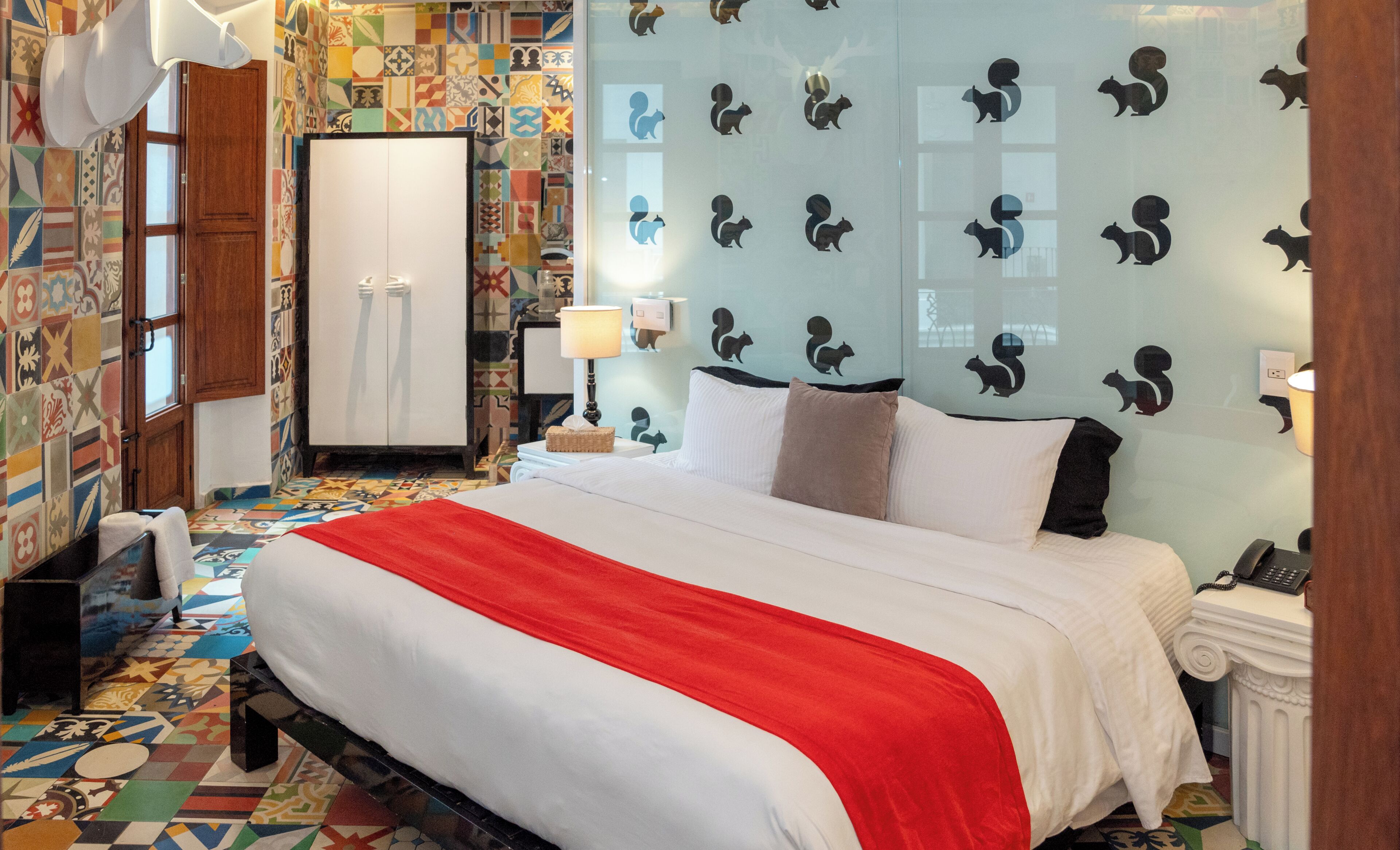 Una habitación de hotel con una cama grande, un armario, un escritorio con lámpara y una pared decorada con motivos de animales.