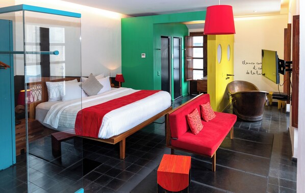 Una habitación de hotel moderna con una cama grande, un sofá rojo, una lámpara roja y un espejo grande.