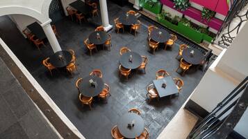 Una terraza en la azotea con varias mesas y sillas redondas, rodeada por un muro blanco y una jardinera verde con plantas.