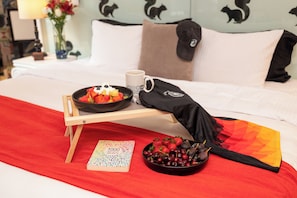 A bed with a tray holding a bowl of fruit, a mug, and a book titled '1000 Things You Don't Know About Me'. - Del Carmen Concept Hotel (Guadalajara)