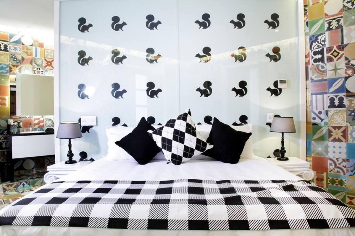 A hotel room with a checkered bedspread, black and white patterned pillows, and a wall decorated with animal silhouettes.
