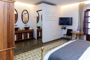 A hotel room with a bed, a television, a desk, and a bathroom with a mirror and sink. - Del Carmen Concept Hotel (Guadalajara)