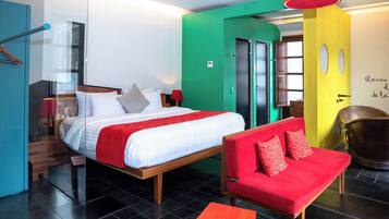 Habitación de hotel con cama, sofá rojo, mesa de madera y baño con pared amarilla.