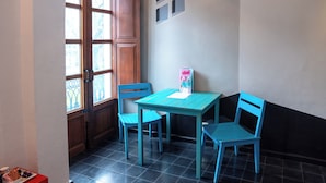 A small room with a wooden door, a window, a table with chairs, and a wall-mounted shelf. - Del Carmen Concept Hotel (Guadalajara)