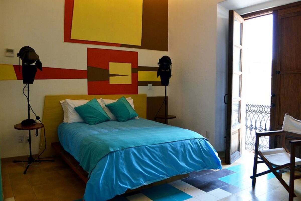 A bedroom with a bed, two bedside lamps, a chair, a door, and a window.
