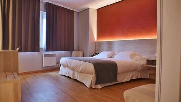 Una habitación de hotel moderna con una cama grande, una mesita de noche, una silla y una ventana con cortinas.