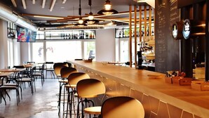 A bar area with a long counter, multiple stools, and a barista station. - Hospedium Hotel La Marina (Cee)
