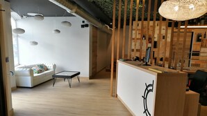 A modern reception area with a wooden desk, a sofa, and hanging pendant lights. - Hospedium Hotel La Marina (Cee)