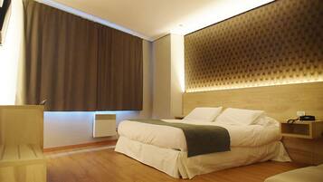 Une chambre d’hôtel moderne avec un grand lit, une tête de lit en bois, une table de chevet et une grande fenêtre avec des rideaux.