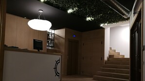 A modern interior with a reception desk, wooden flooring, a staircase, and a ceiling with a green plant installation. - Hospedium Hotel La Marina (Cee)