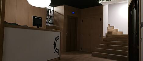 A modern interior with a reception desk, wooden flooring, a staircase, and a ceiling with a green plant installation.