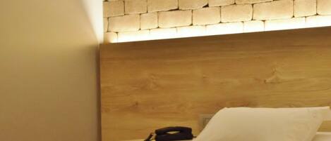 Habitación de hotel con cabecera de ladrillo, cama con ropa blanca y mesita de noche con un teléfono.