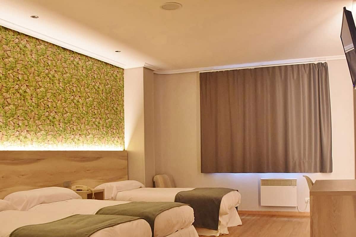Una habitación de hotel con dos camas, cabecera de madera, televisor de pantalla plana, ventana con cortinas y aire acondicionado instalado en la pared.