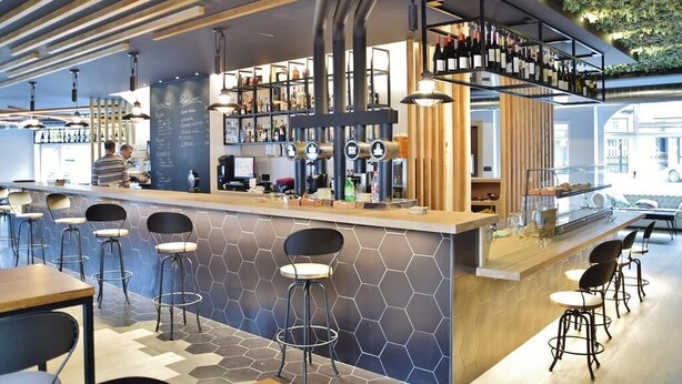 A modern bar area with hexagonal patterned walls, a wooden counter, and a wine display. - Hospedium Hotel La Marina (Cee)