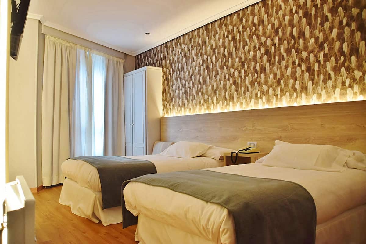 Habitación de hotel con dos camas, un armario, una mesita de noche y una pared con textura.