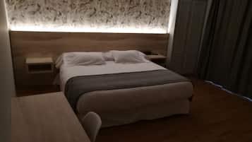 Een moderne hotelkamer met een houten hoofdbord, een bed met witte lakens, een nachtkastje en een bijzettafeltje.