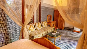 Una habitación con piso estampado, un sofá con cojines, una mesita con un jarrón y una cama con dosel.