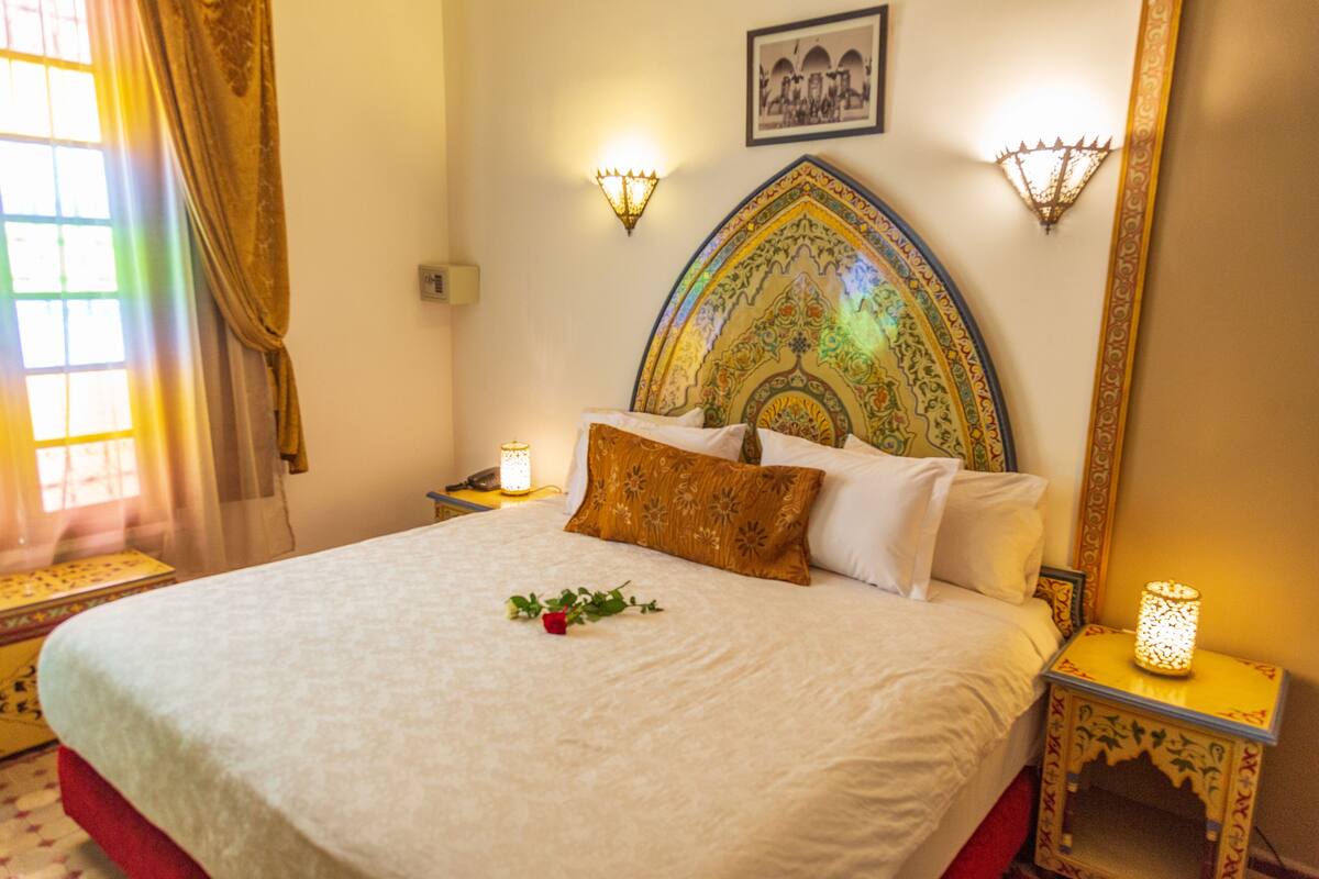 A neatly made bed with a decorative headboard, two bedside lamps, and a framed picture on the wall.
