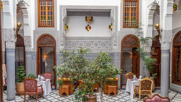Un patio con zona de comedor, plantas en macetas y detalles arquitectónicos ornamentales.