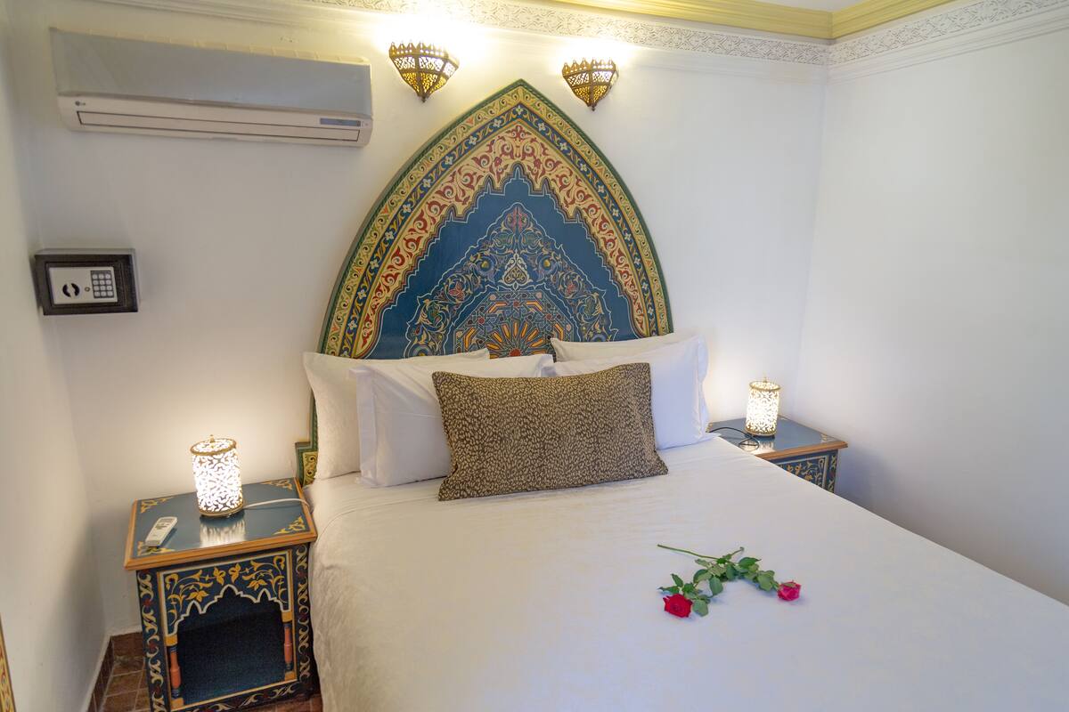 A neatly made bed with a decorative headboard, two bedside tables with lamps, and a wall-mounted air conditioner.