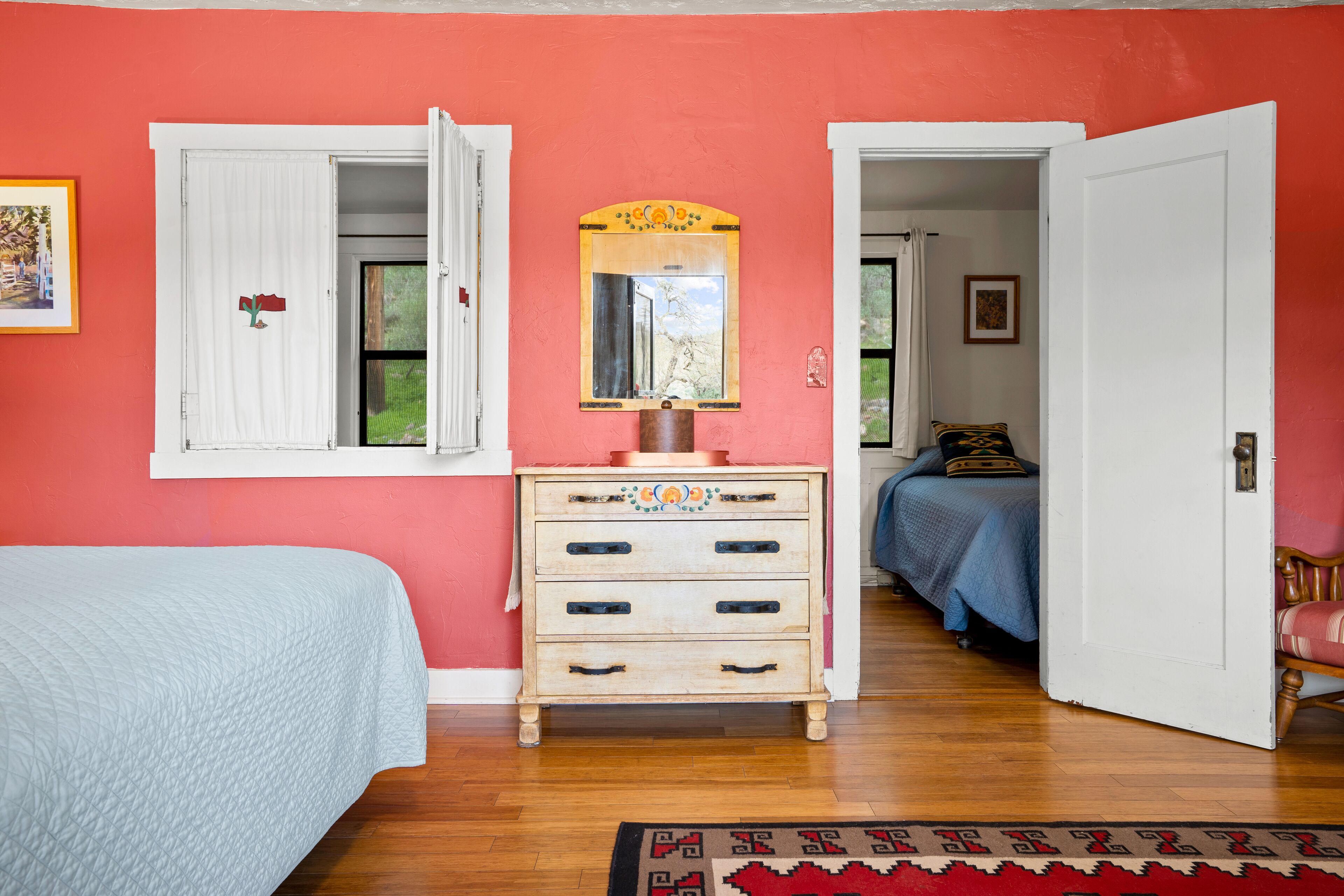 A bedroom with a bed, a dresser, a mirror, and a door leading to another room.