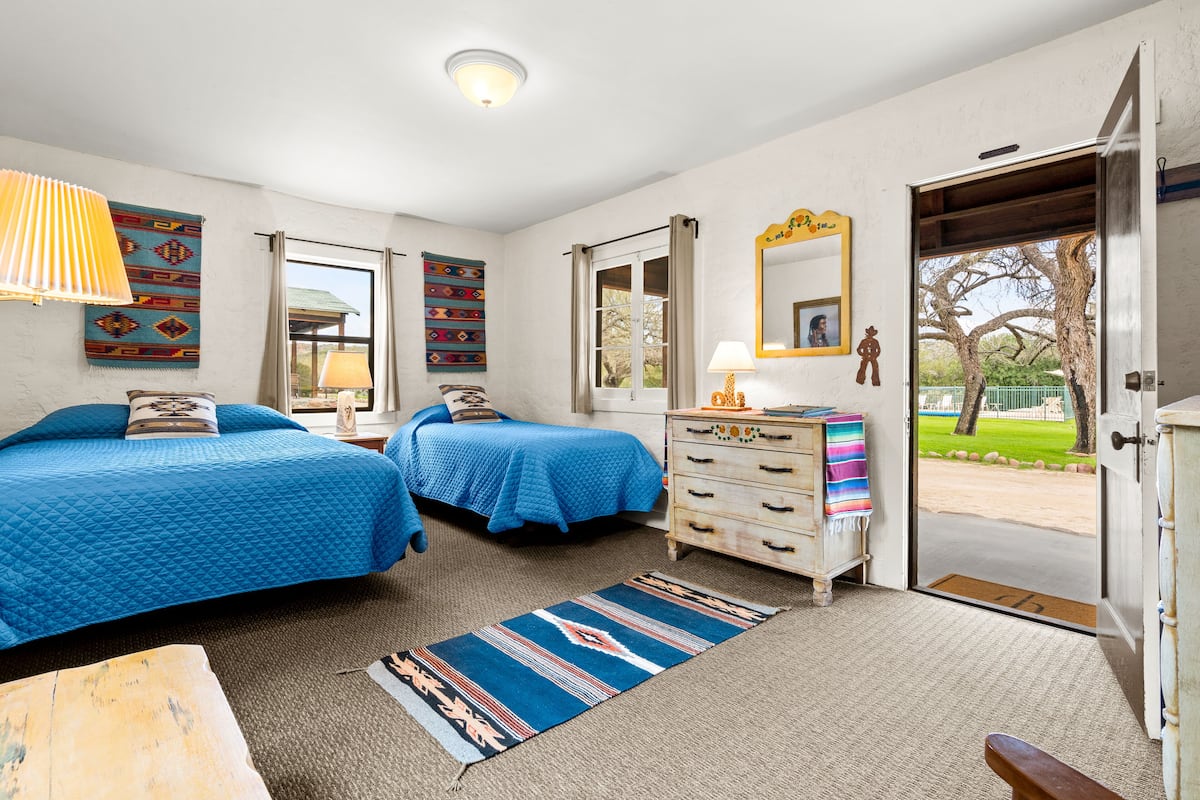 A room with two beds, a dresser, a mirror, and a door leading outside.