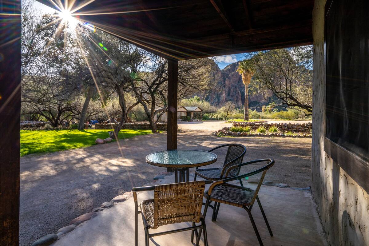 A covered patio with a glass table and wicker chairs, overlooking a landscaped garden and a mountain backdrop.