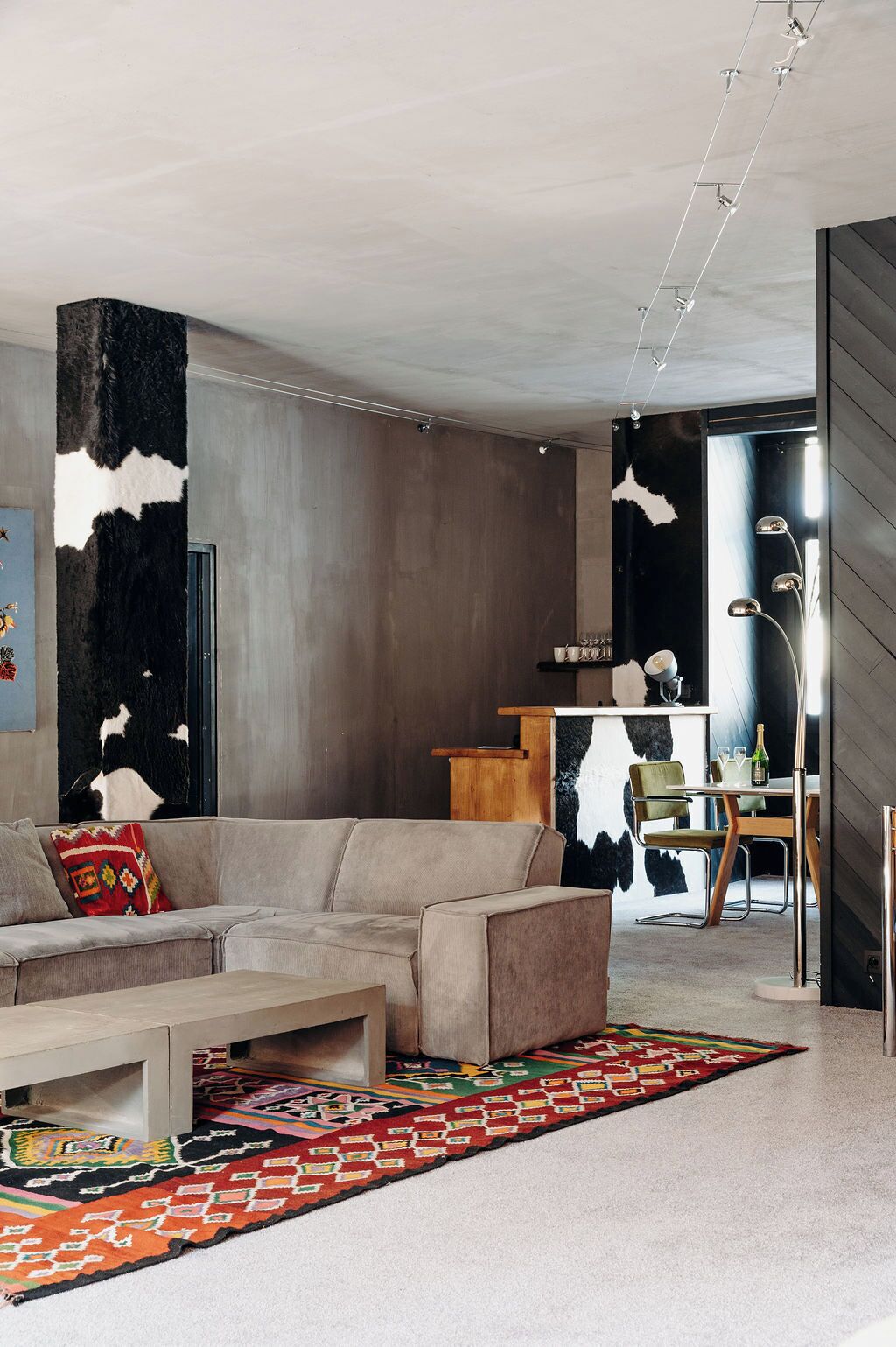 A modern living room with a sofa, a coffee table, a patterned rug, a wooden side table, and a black and white cowhide artwork on the wall.