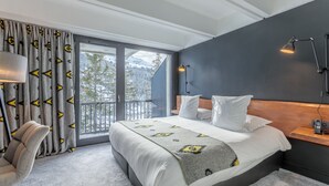 A modern bedroom with a large bed, a view of mountains through the window, a balcony, and a desk with a lamp. - Totem, Friendly Hotel (Araches-la-Frasse)