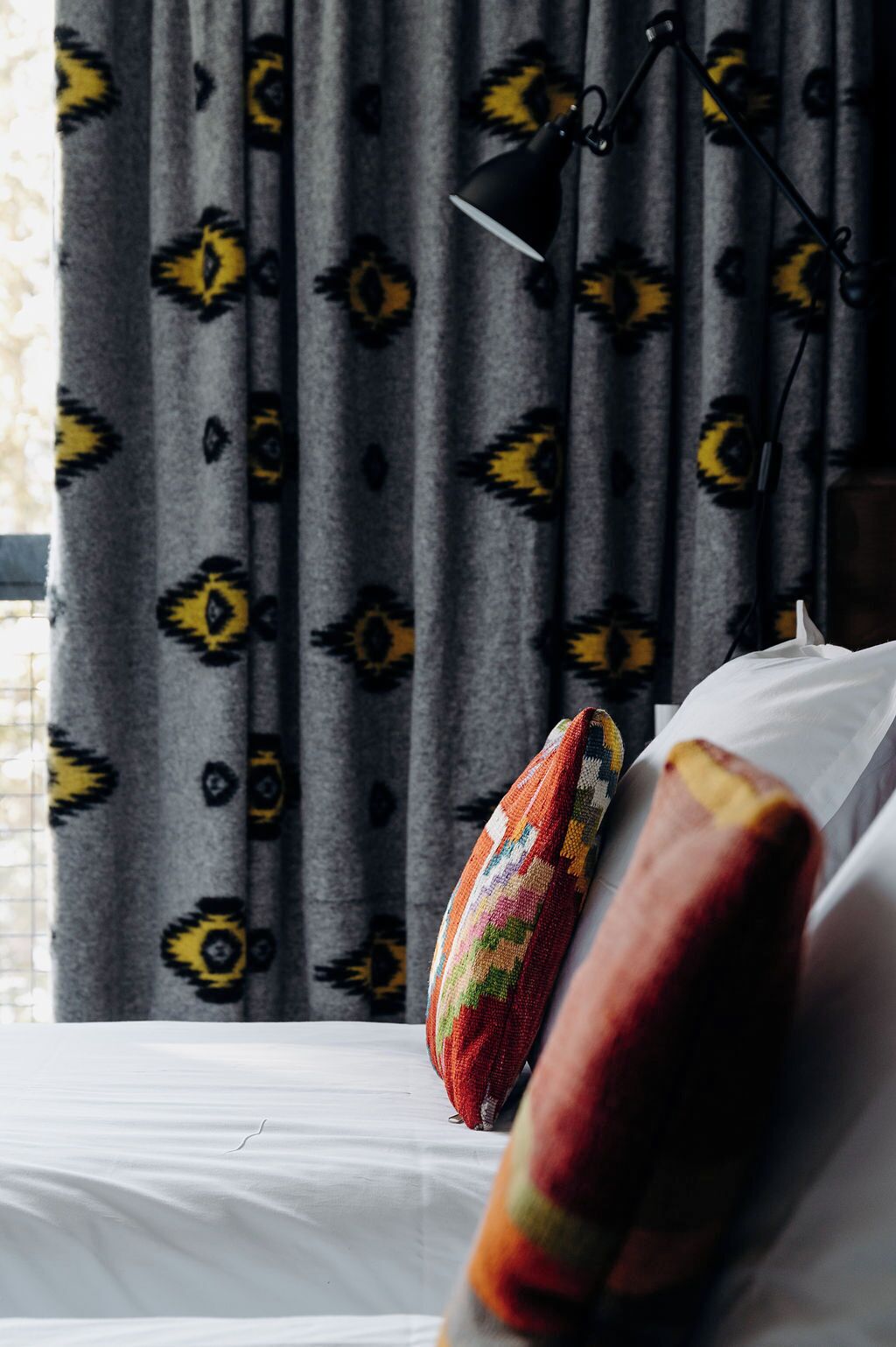 A bed with a colorful blanket and a black lamp on a bedside table.