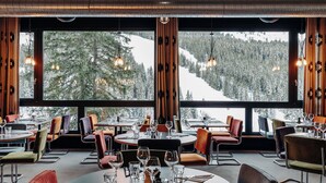 A restaurant with round tables, chairs, and hanging light fixtures. Large windows offer a view of a snowy mountain. - Totem, Friendly Hotel (Araches-la-Frasse)