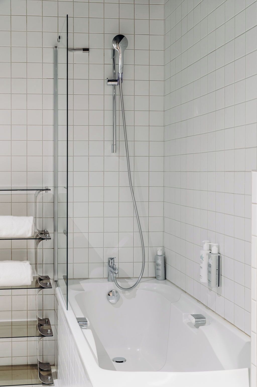 A modern bathroom with a glass-enclosed shower, a white bathtub, and a built-in shelf with towels.