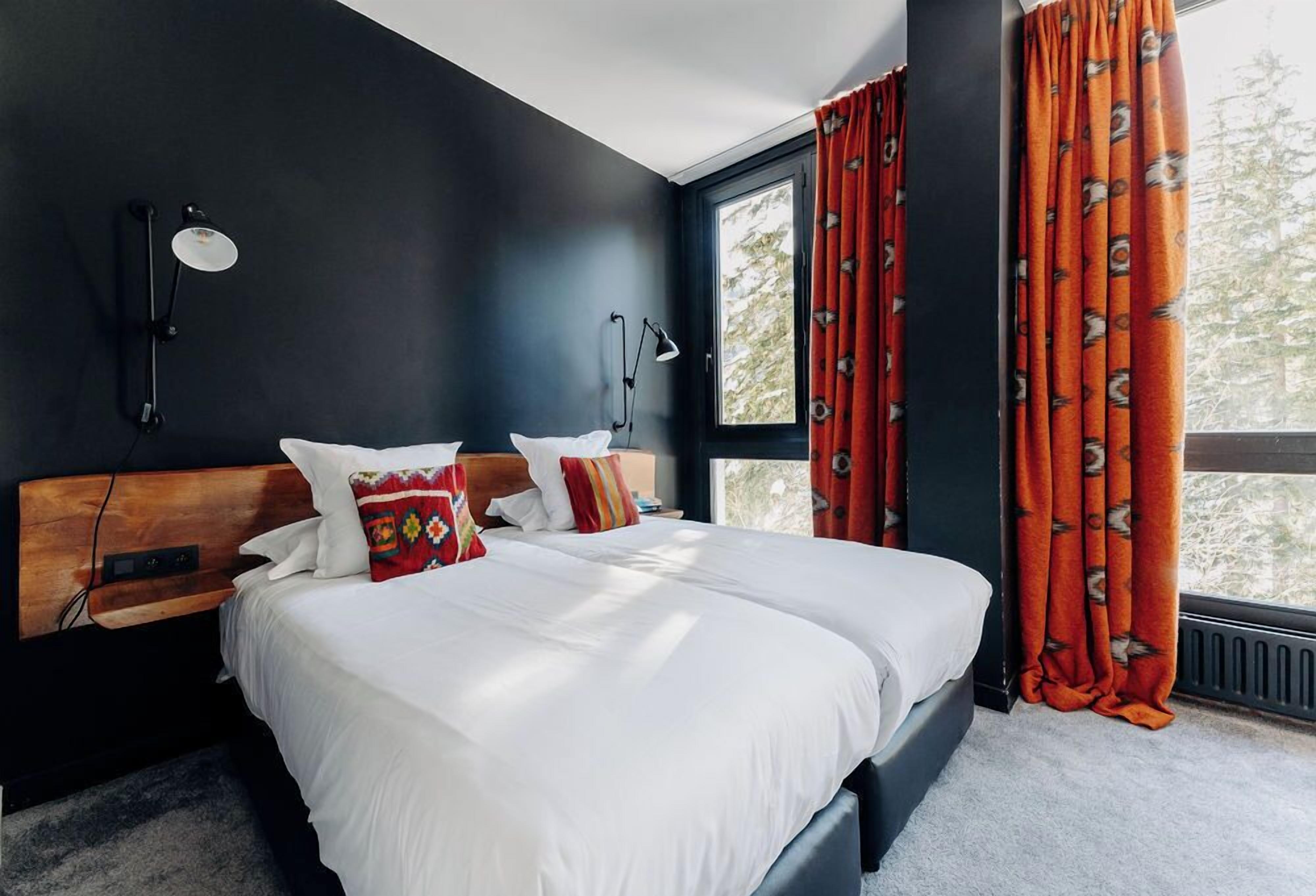 A modern bedroom with a large bed, two bedside lamps, and a window with curtains.