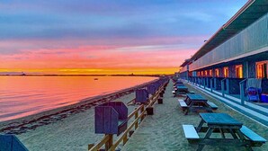 A beachside hotel with a row of beach chairs and tables, a wooden deck, and a view of the ocean at sunset. - Top Mast Resort (North Truro)