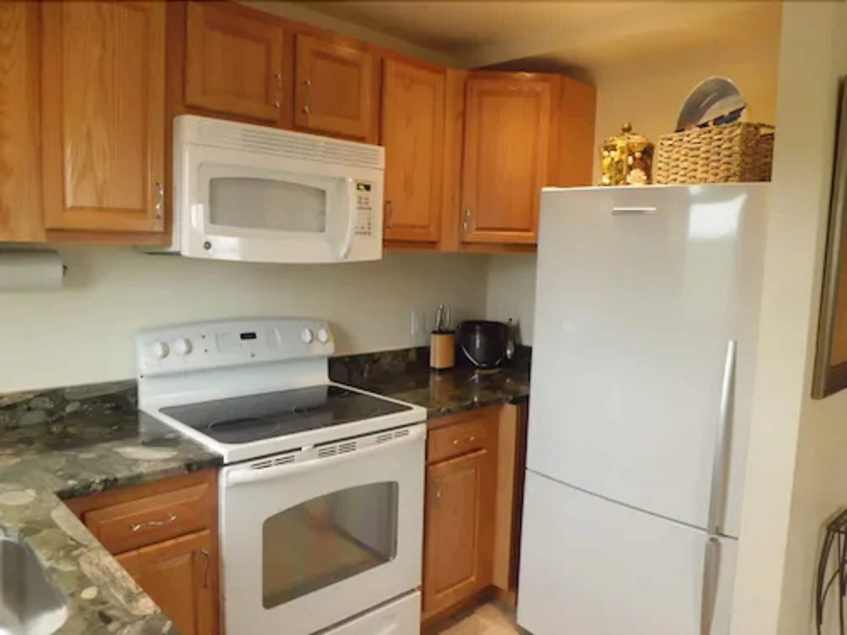 A kitchen with wooden cabinets, a white microwave, a stove, and a refrigerator.