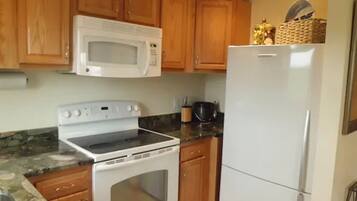 A kitchen with wooden cabinets, a white microwave, a stove, and a refrigerator.