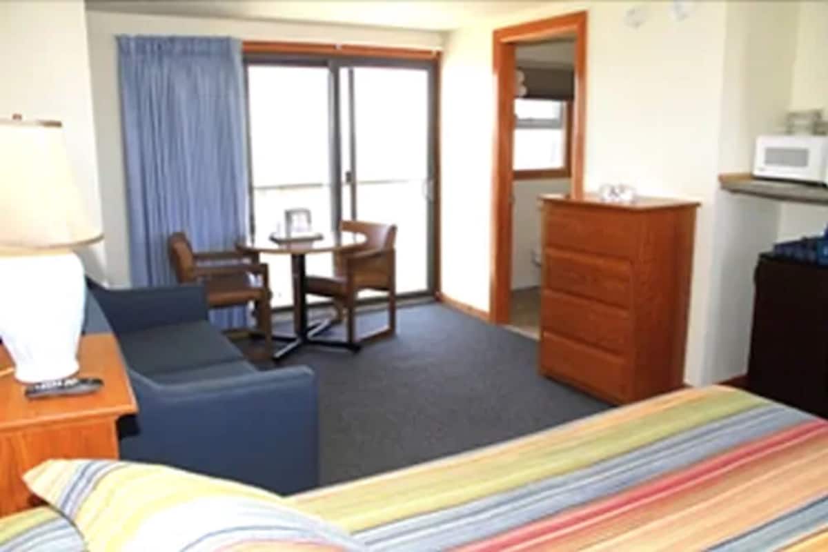 A hotel room with a bed, a desk with a lamp, a chair, a dresser, and a microwave.
