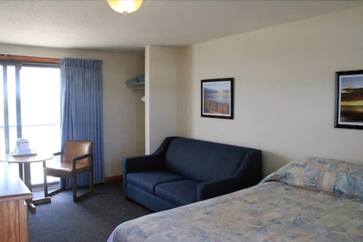 A hotel room with a bed, a sofa, a small table with a chair, and a window with curtains.