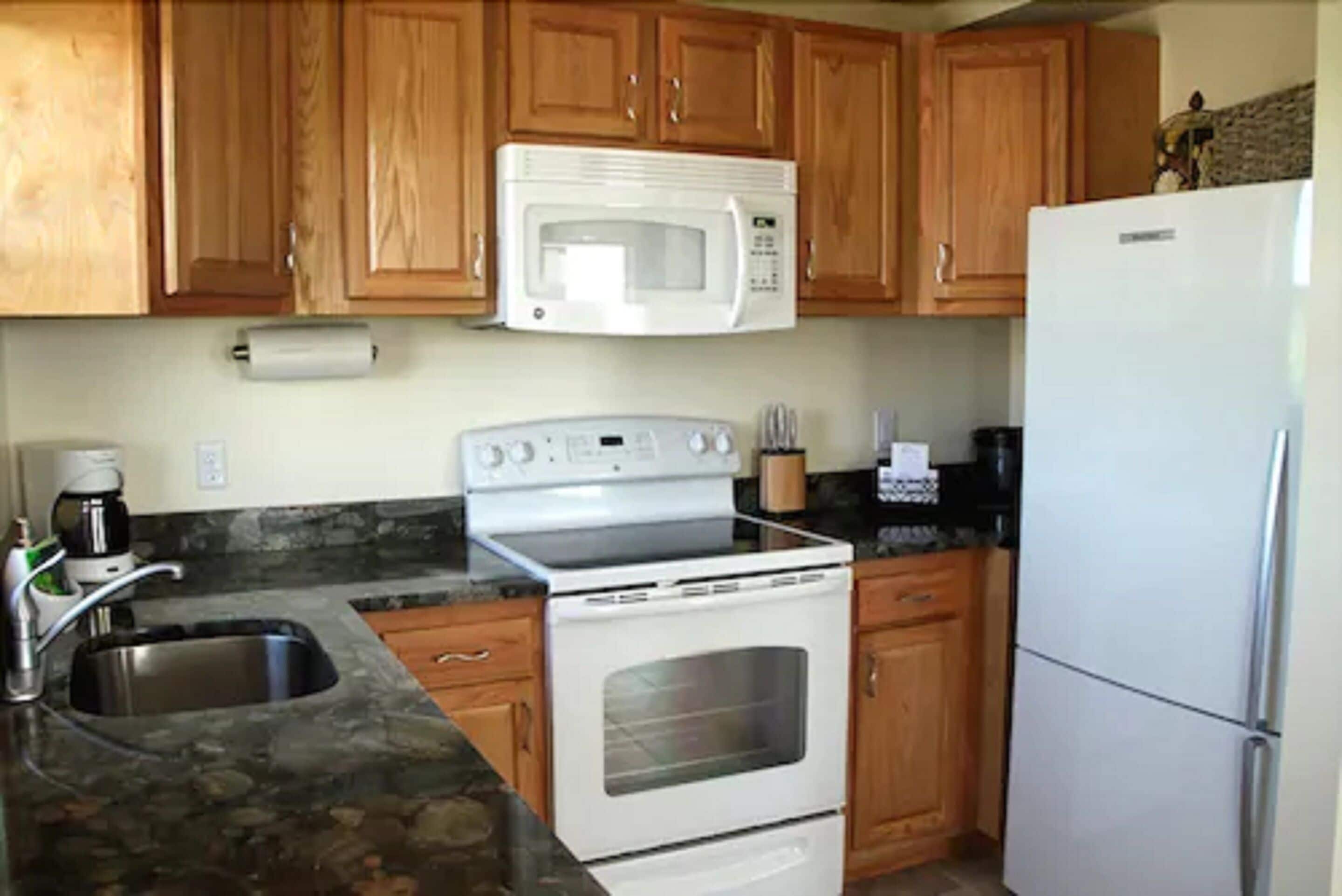 A kitchen with wooden cabinets, a white microwave, a stove, a sink, and a refrigerator.